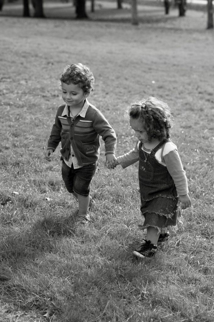 Two young children joyfully holding hands and walking in a grassy field, captured in charming black and white.