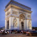 Iconic Arc de Triomphe under blue evening sky with bustling traffic in Paris.