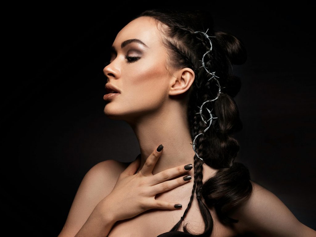 Captivating studio portrait featuring a woman with braided hair adorned with barbed wire, set against a dark background.