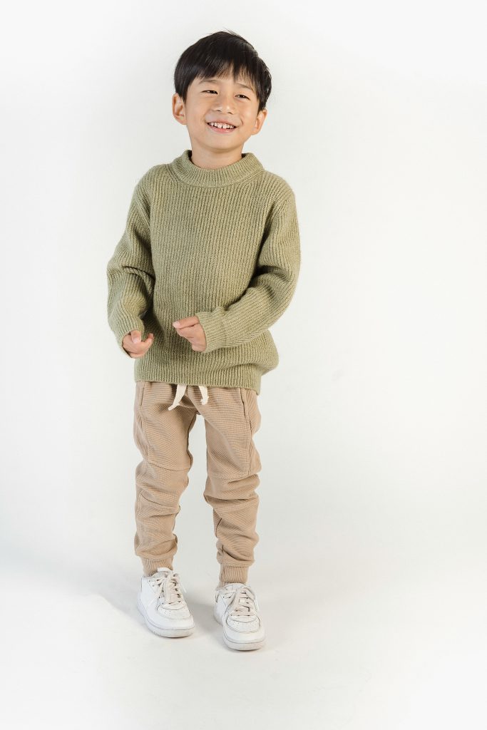 Happy child in a warm sweater standing and smiling on a white background.