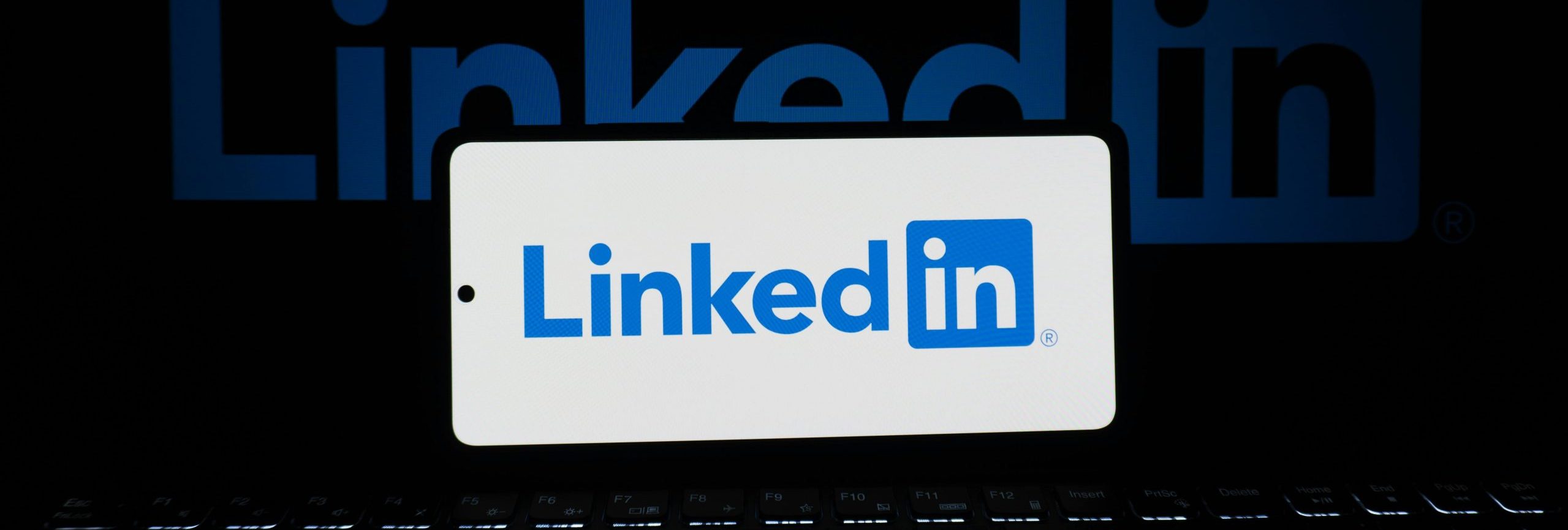 Smartphone showing LinkedIn logo with keyboard and large background logo, business theme.
